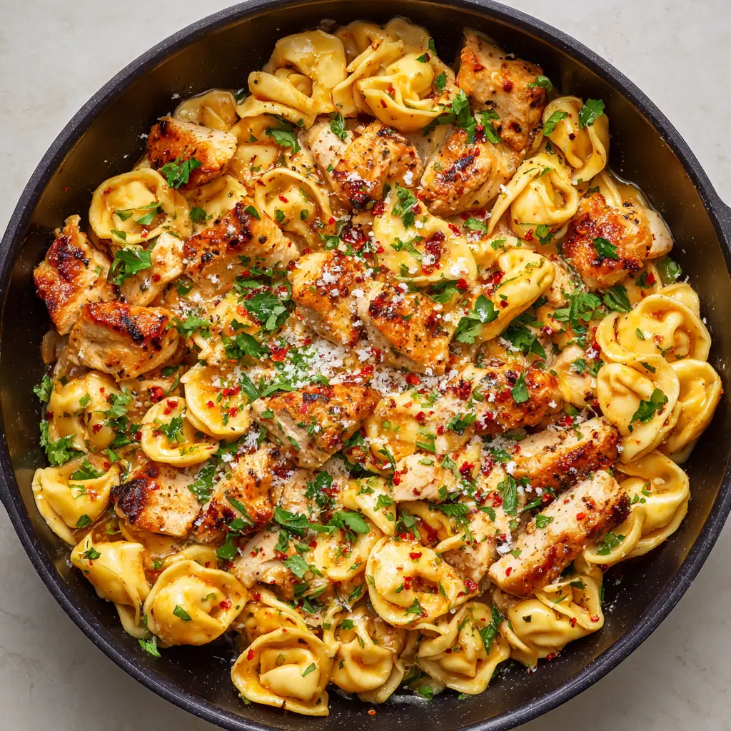 Spicy Garlic Butter Chicken Tortellini: The Ultimate Cast-Iron Skillet Recipe 1 A cast-iron skillet filled with cheese tortellini, chicken, bright red pepper flakes, fine white Parmesan cheese, and vibrant green parsley.