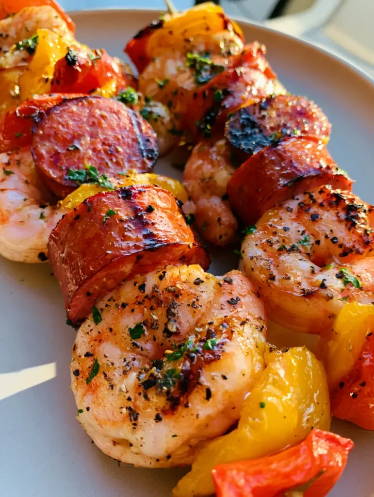 Grilled Shrimp and Sausage Skewers with Blistered Peppers and Herb Glaze 1 Overhead view of grilled seafood skewers with charred smoked sausage rounds and vibrant blistered bell peppers sprinkled with fresh parsley.