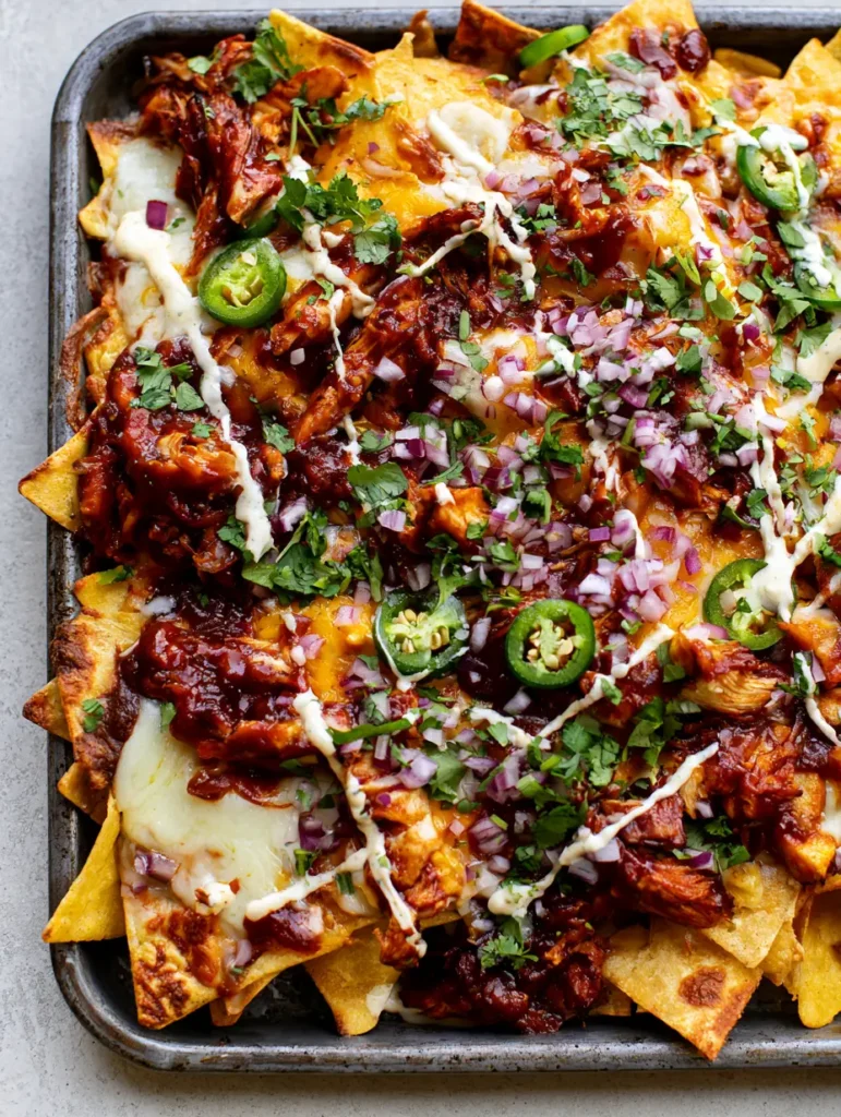 Rustic metal tray overflowing with BBQ Chicken Nachos garnished with jalapeños, red onions, and cilantro.