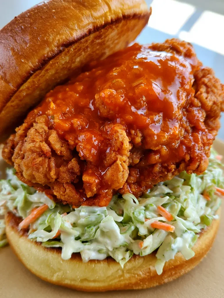 A Buffalo Chicken Sandwich assembled with thick creamy coleslaw and a tilted brioche bun top.