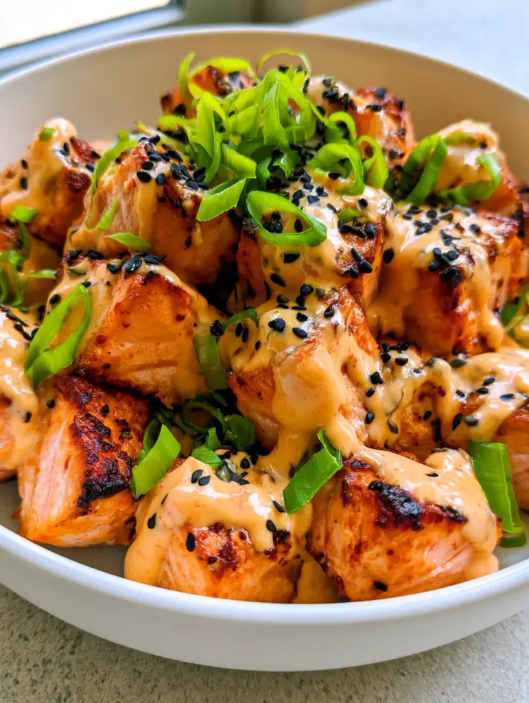 Close-up of glossy Bang Bang sauce drizzled over roasted salmon bites with black sesame seeds.